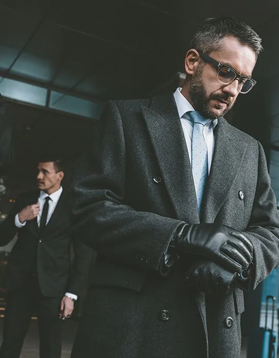 A close protection officer in a dark coat and gloves