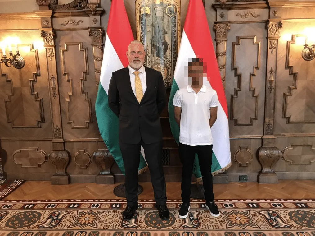 Beau Emms beside the young son of an overseas Head of State, in front of Hungarian flags