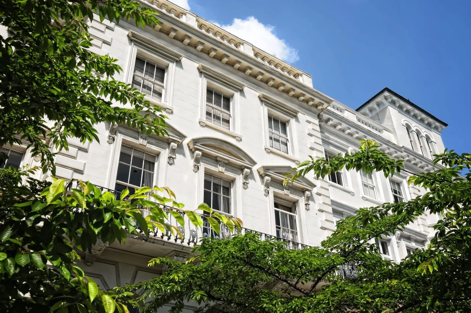 The upper floors of a white stuccoed London terrace, seen through summer trees