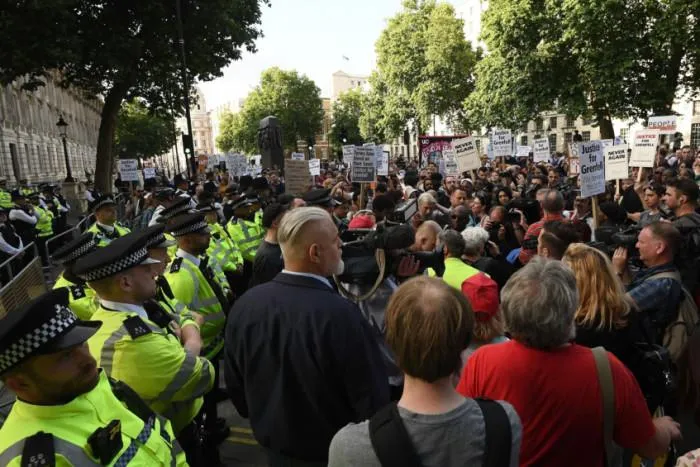 Police officers in high-visibility jackets lining a London street beside a crowd of protesters holding placards
